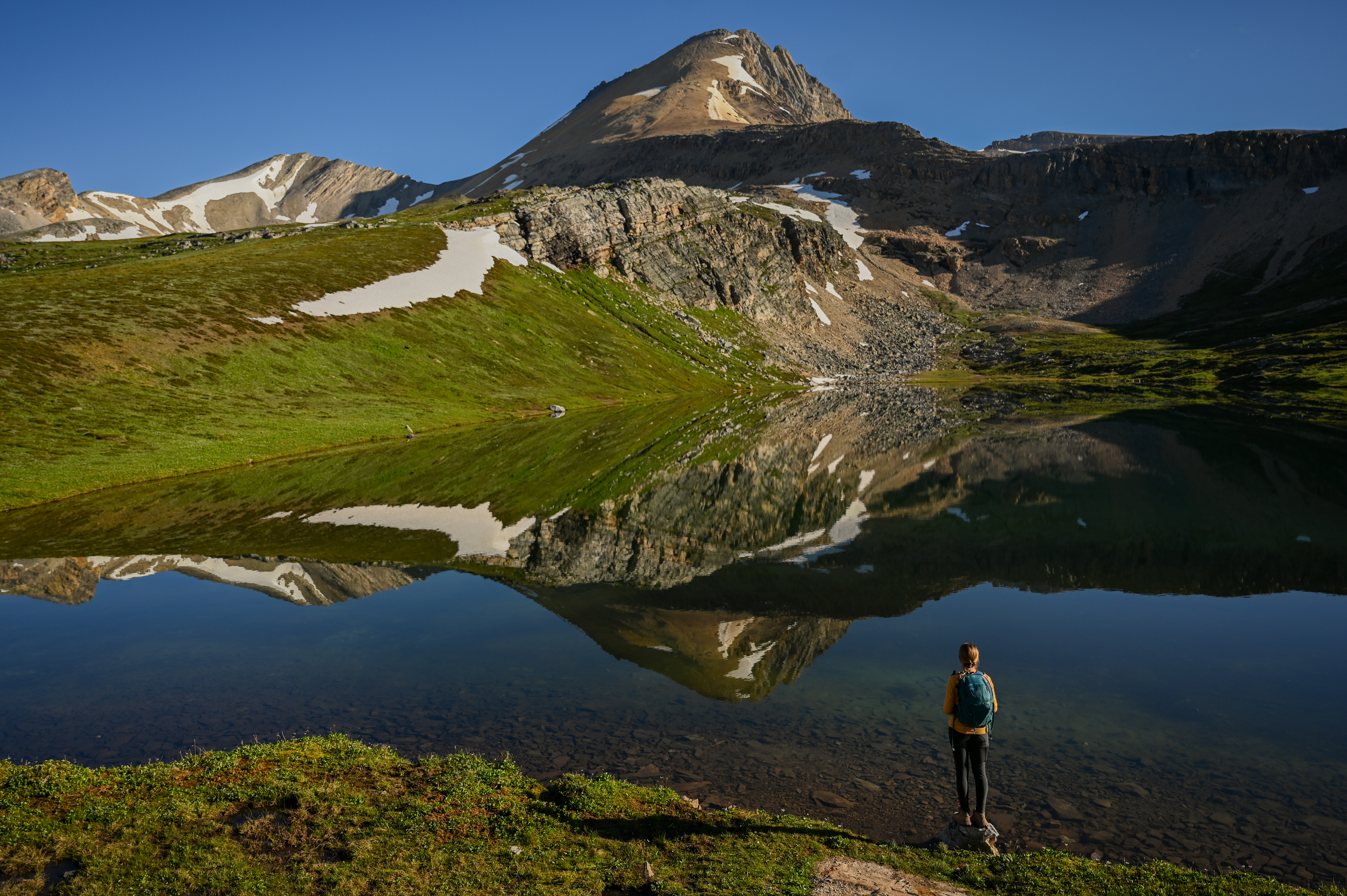 A hiker stands on the shores of Helen Lake below Cirque Peak